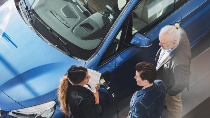 A group of people are looking at a blue car in a showroom.