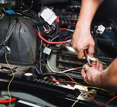 A man is working on a car engine with a pair of pliers.