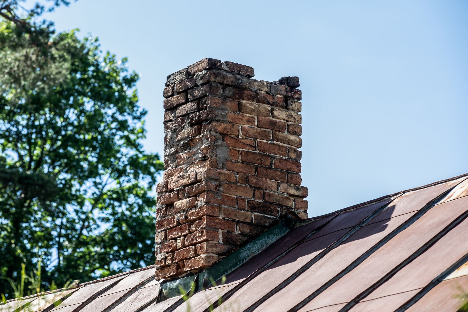 An old chimney on the roof with trees behind, urgently requiring chimney dismantling services.