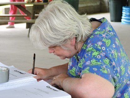 Woman in blue floral shirt writing on papers at a table outdoors