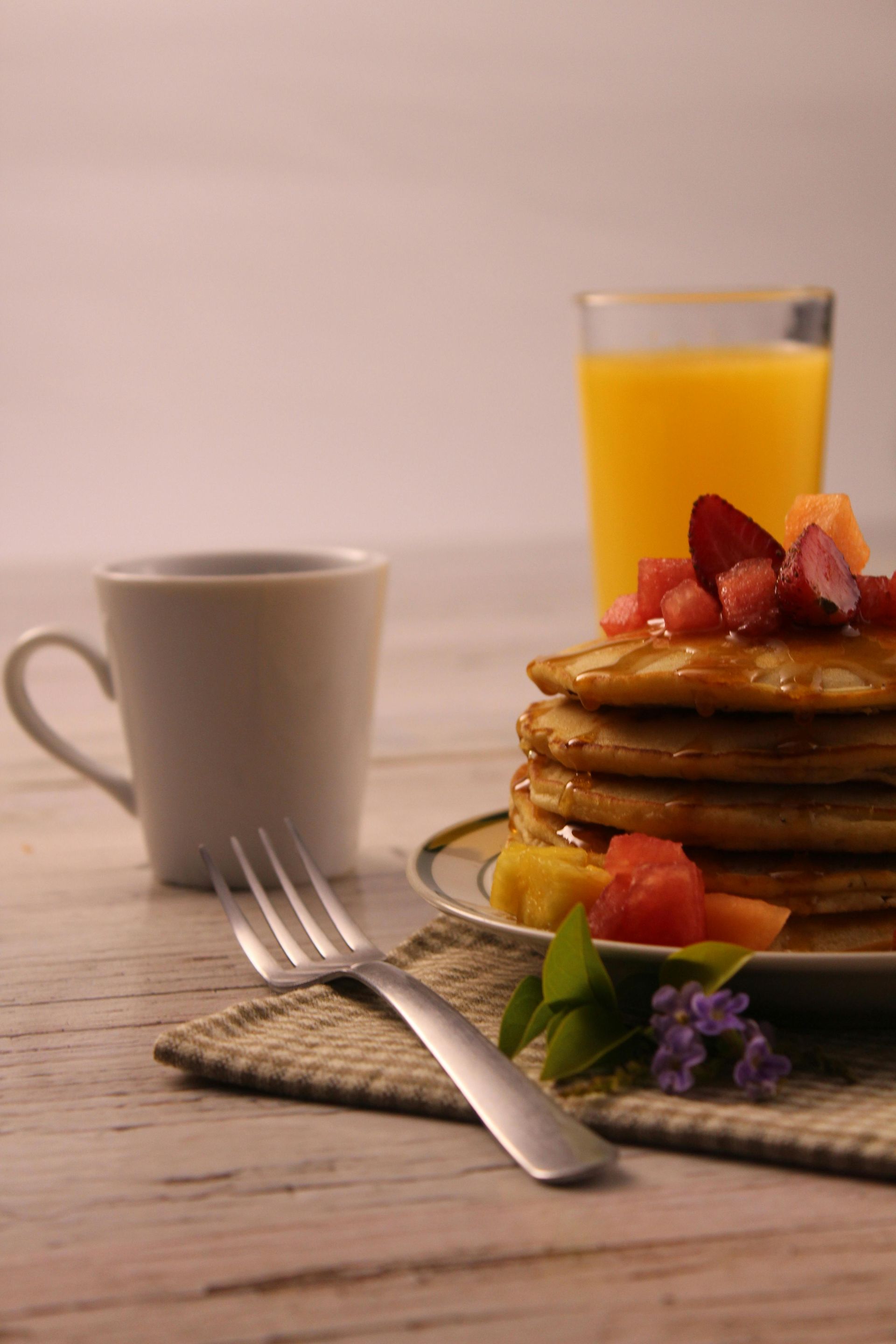 Pancakes with strawberries, orange juice, and a coffee mug on a rustic tablecloth