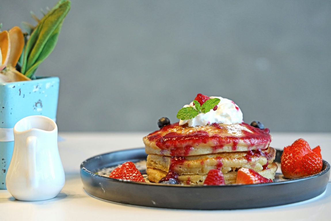 Stack of pancakes topped with strawberries and whipped cream on a blue plate, with a small pitcher beside it