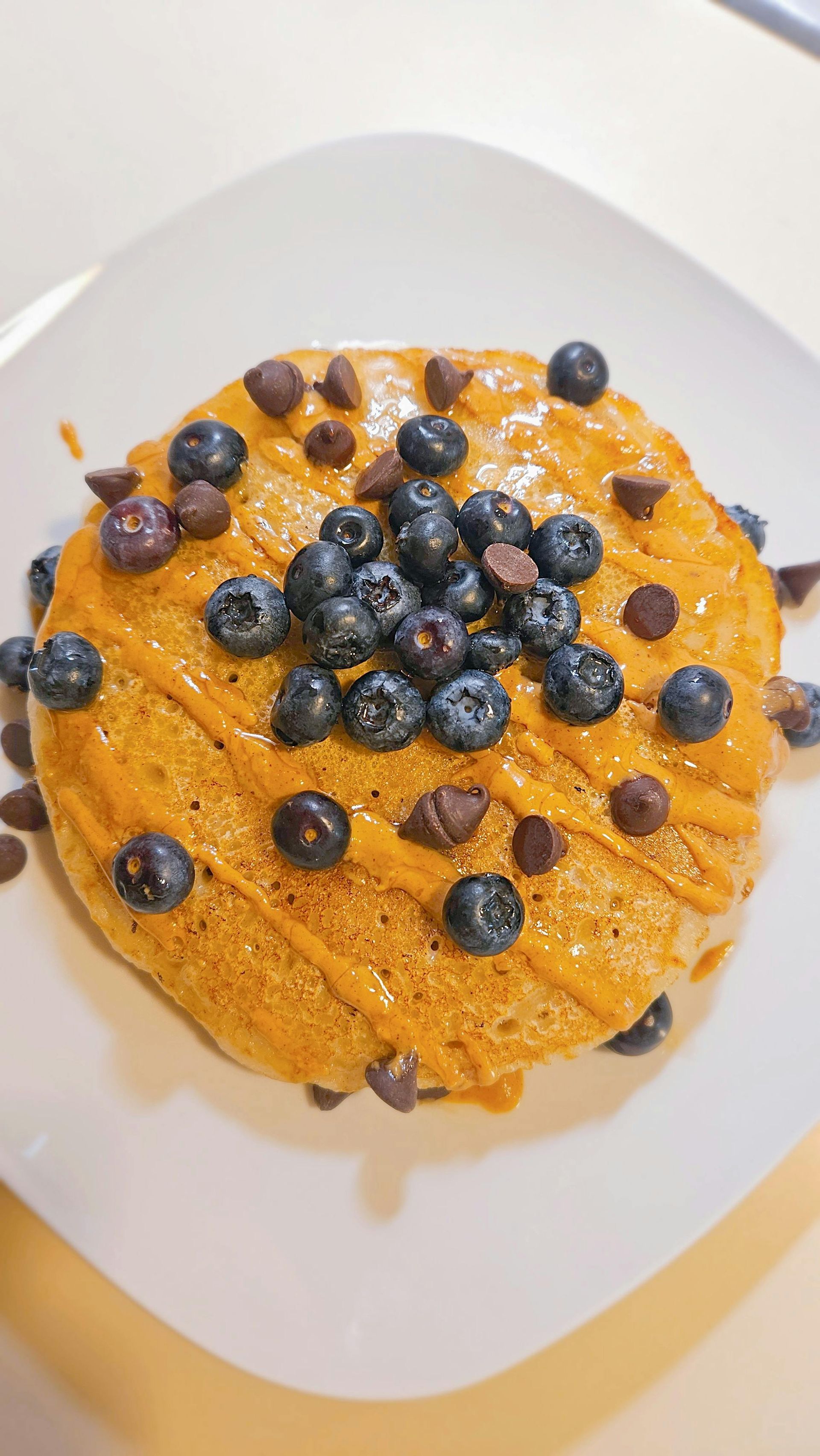 Blueberry-topped stack of golden pancakes on a white plate, drizzled with syrup