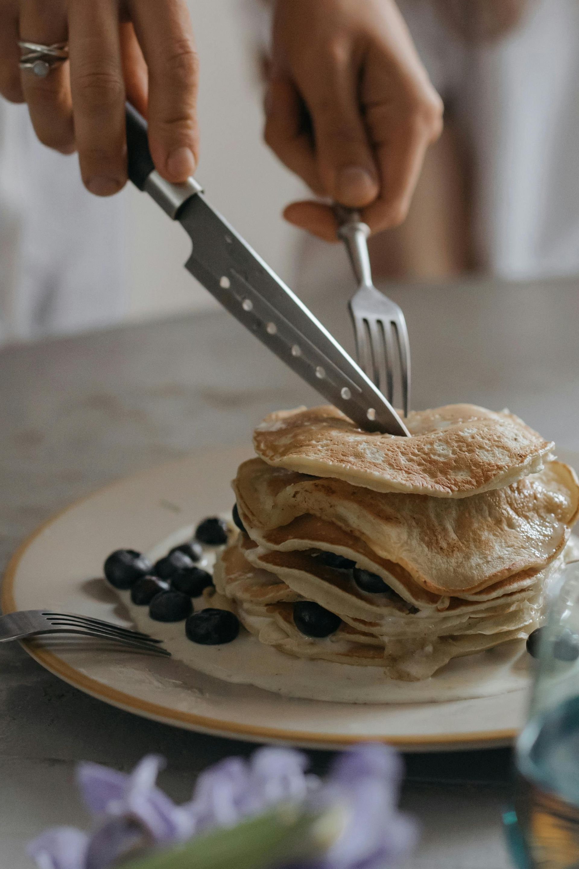 Hands cutting a stack of pancakes with blueberries on a plate
