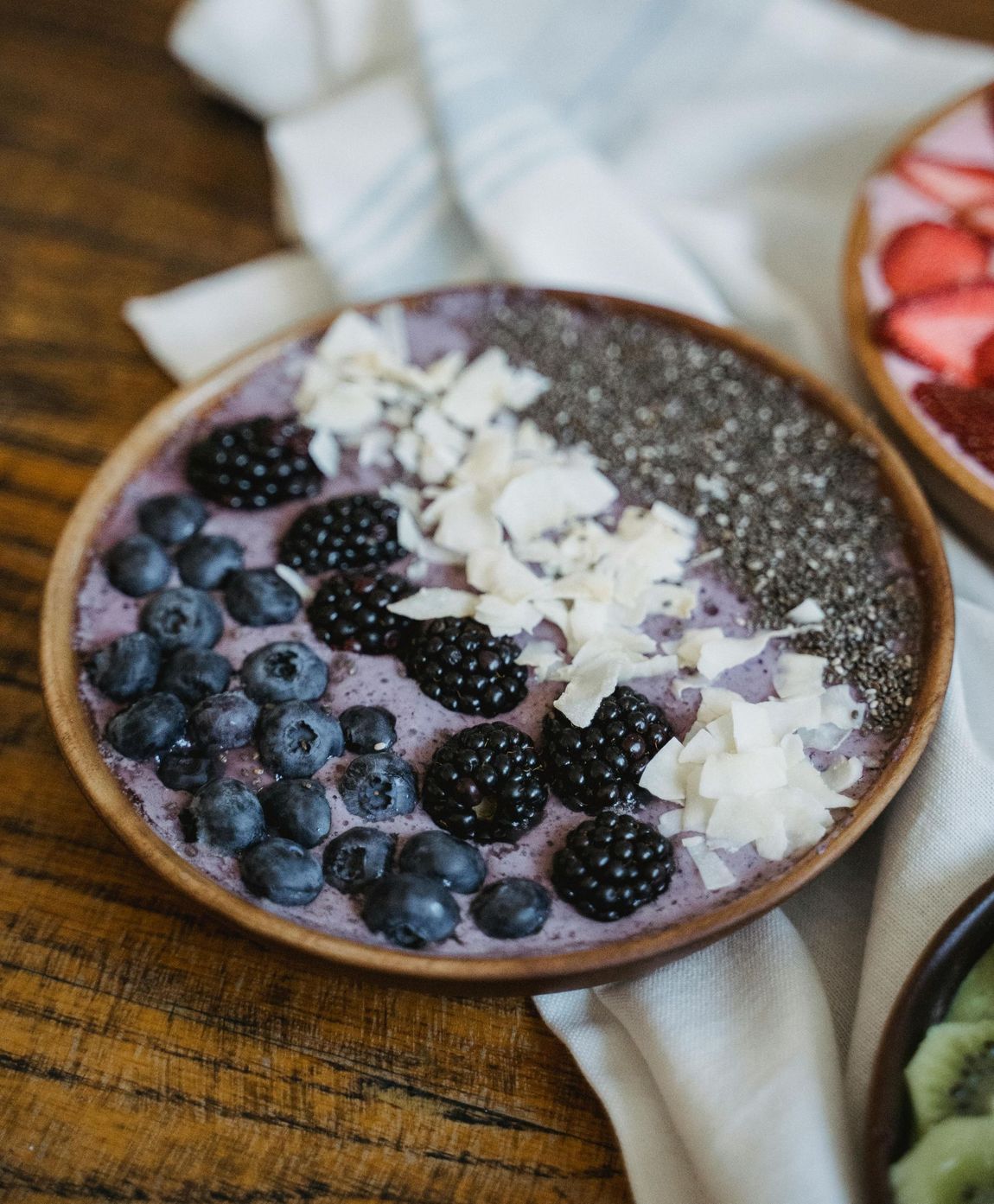 Berry smoothie bowl topped with blueberries, blackberries, coconut flakes, and purple granola on a wooden table