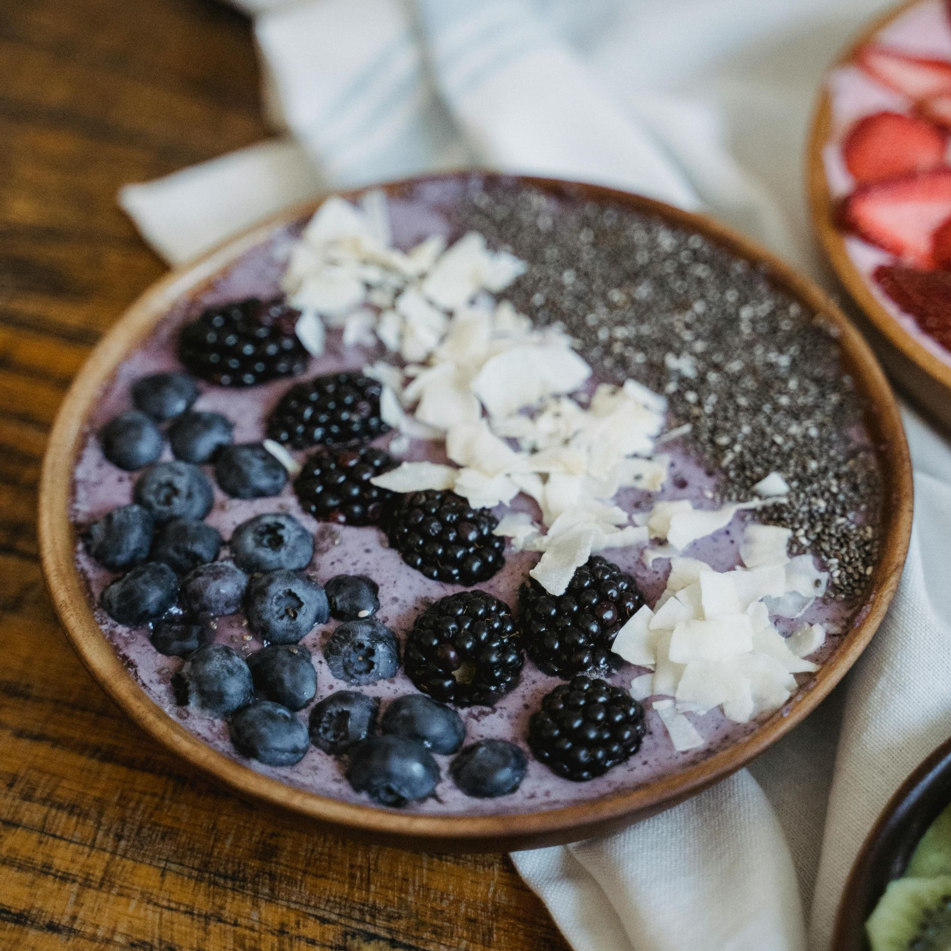 Acai bowl topped with blueberries, blackberries, coconut flakes, and chia seeds on a wooden table