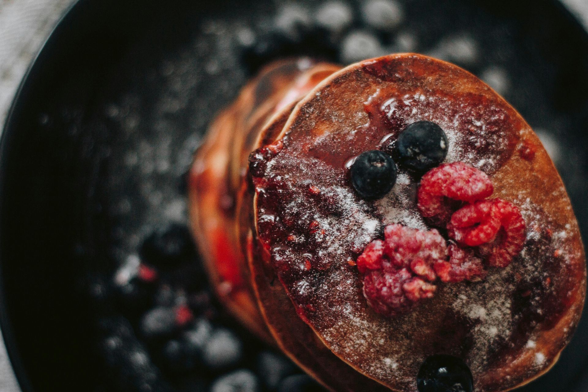 Stack of berry-topped pancakes dusted with powdered sugar on a dark background