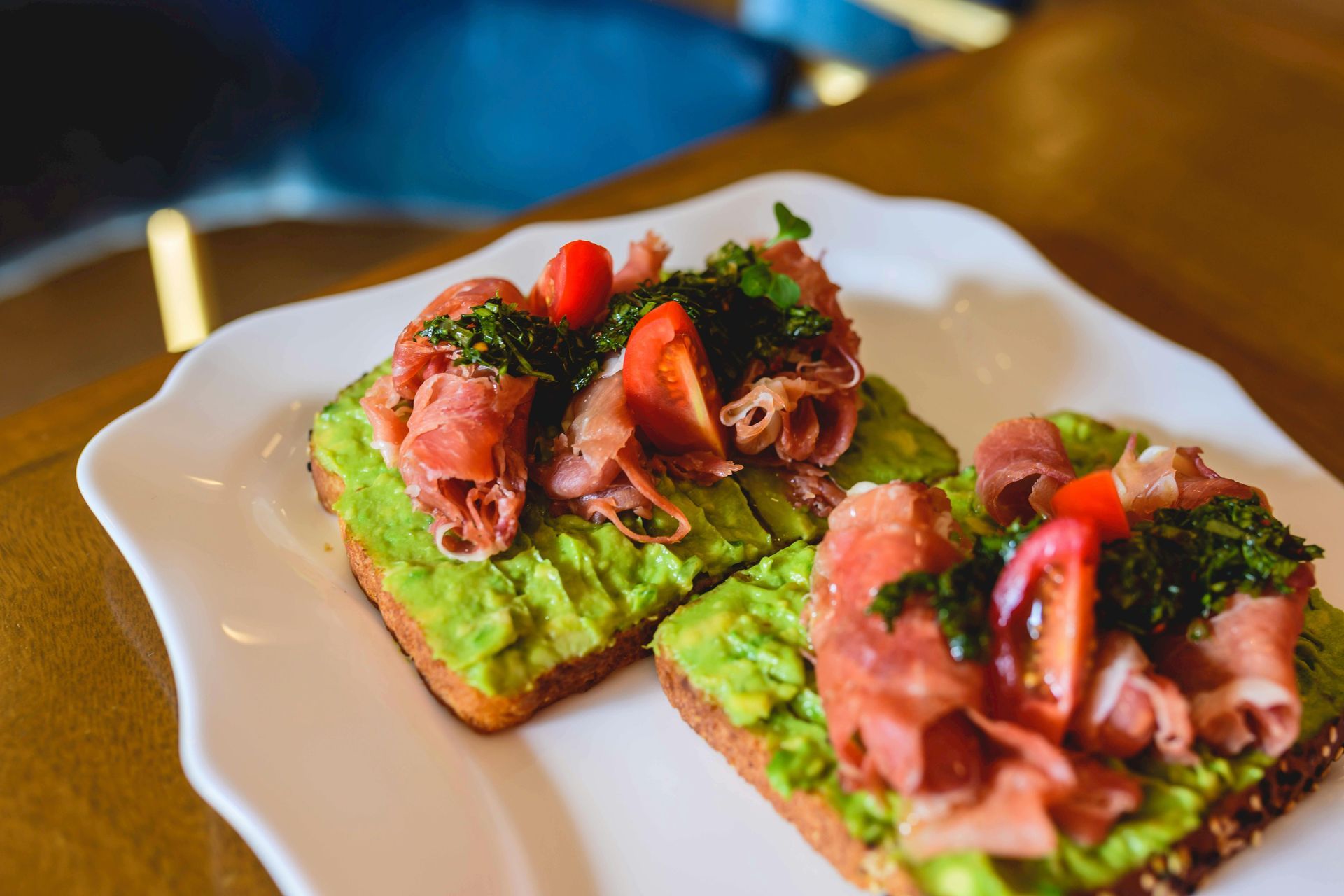 Two avocado toast slices topped with smoked salmon and herbs on a white plate