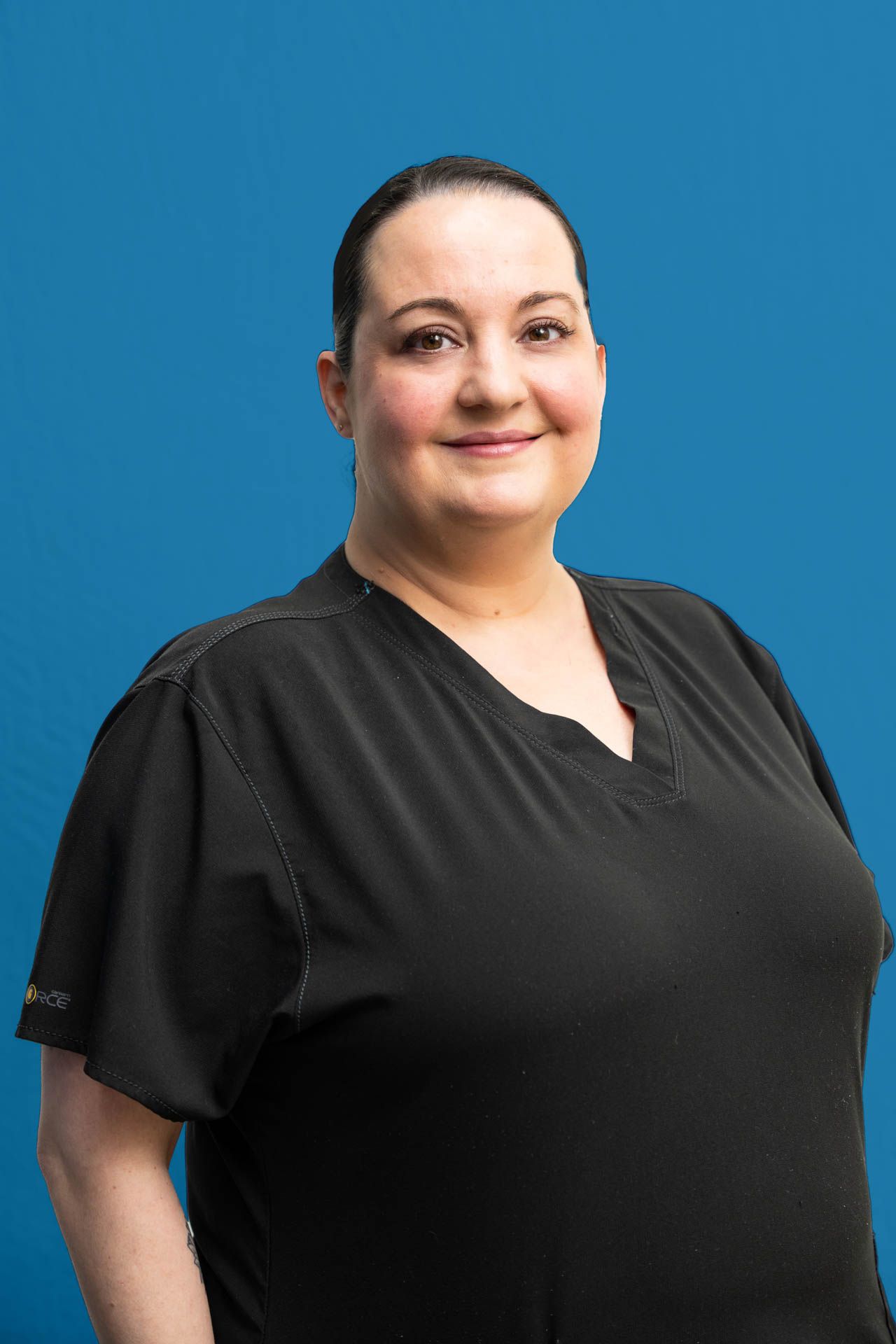 A woman in a black scrub top is standing in front of a blue background.