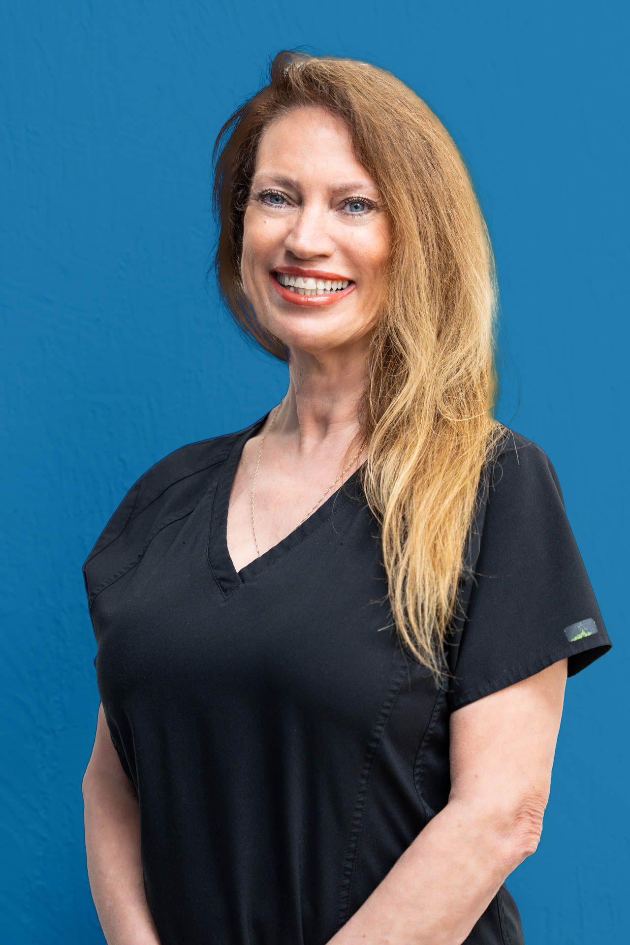 A woman in a black scrub top is smiling and standing in front of a blue background.