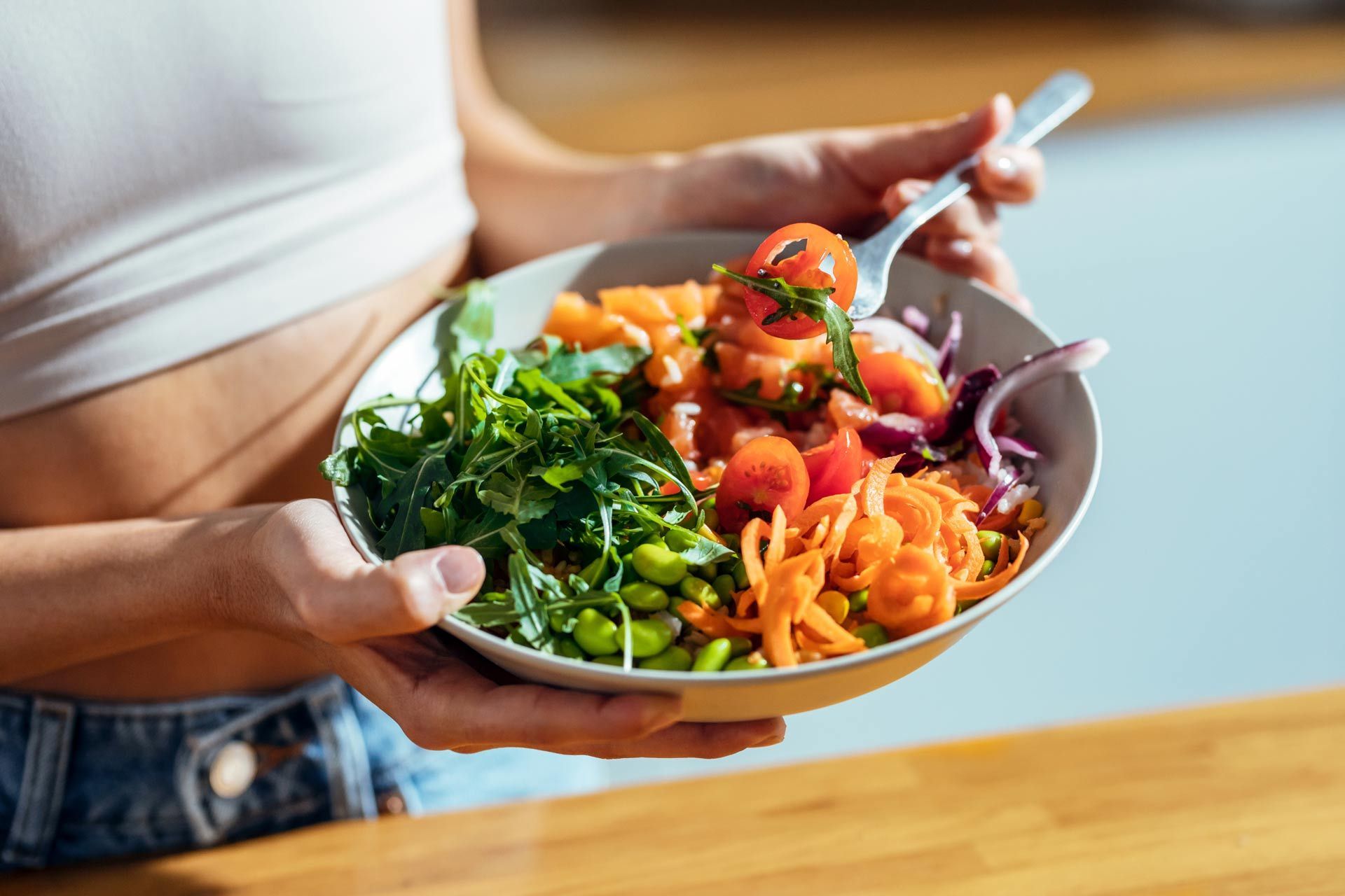 A woman is holding a bowl of vegetables with a fork.
