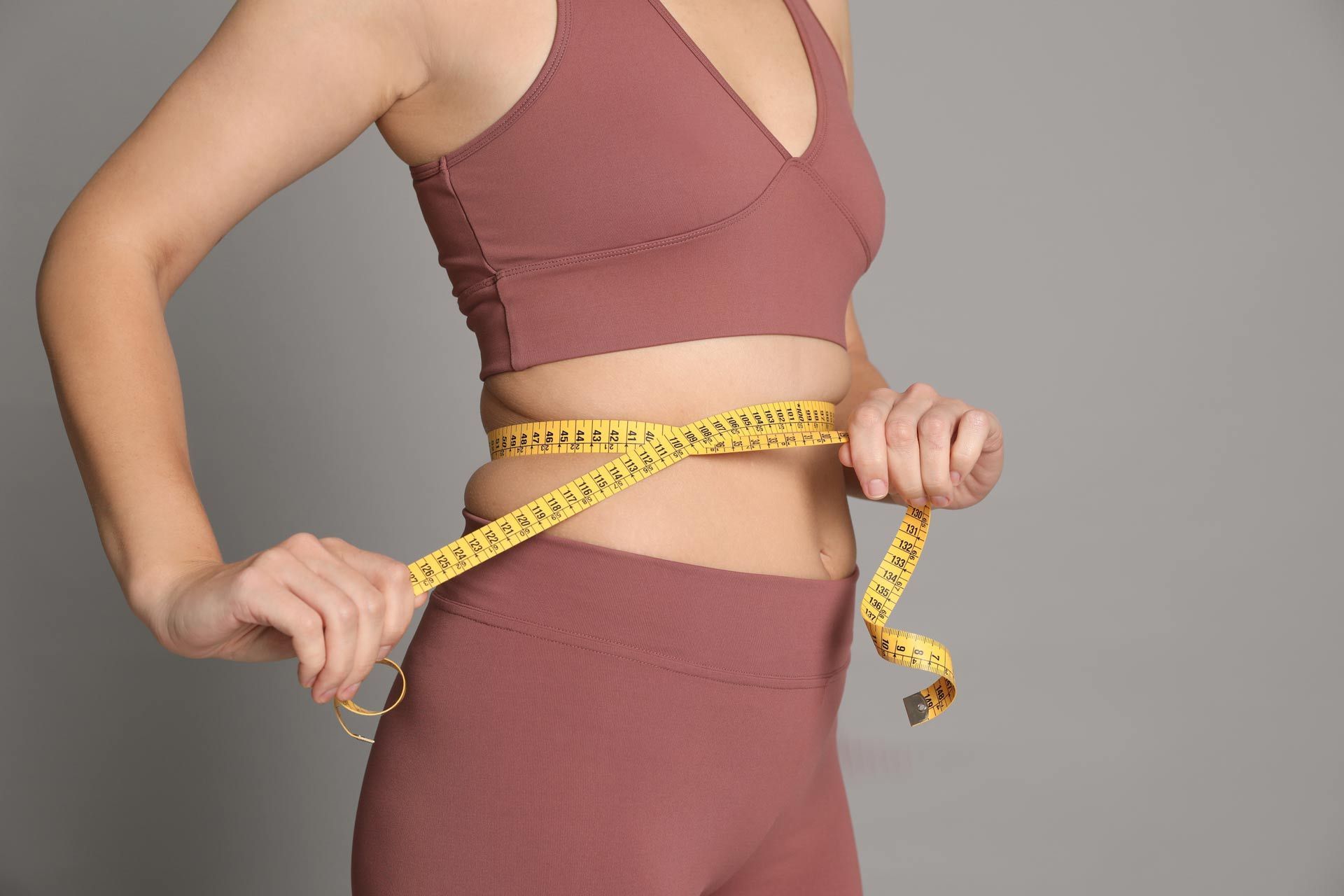 A woman is measuring her waist with a tape measure.
