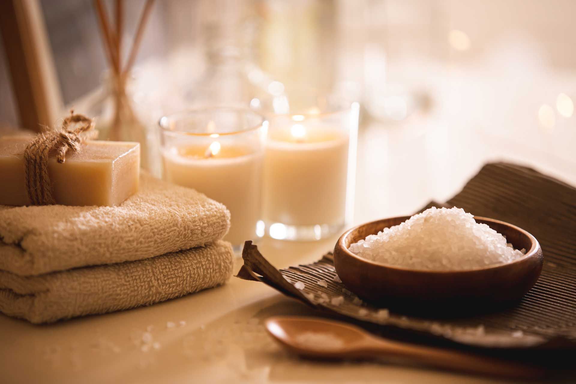 A bowl of sea salt , candles , towels and soap on a table.