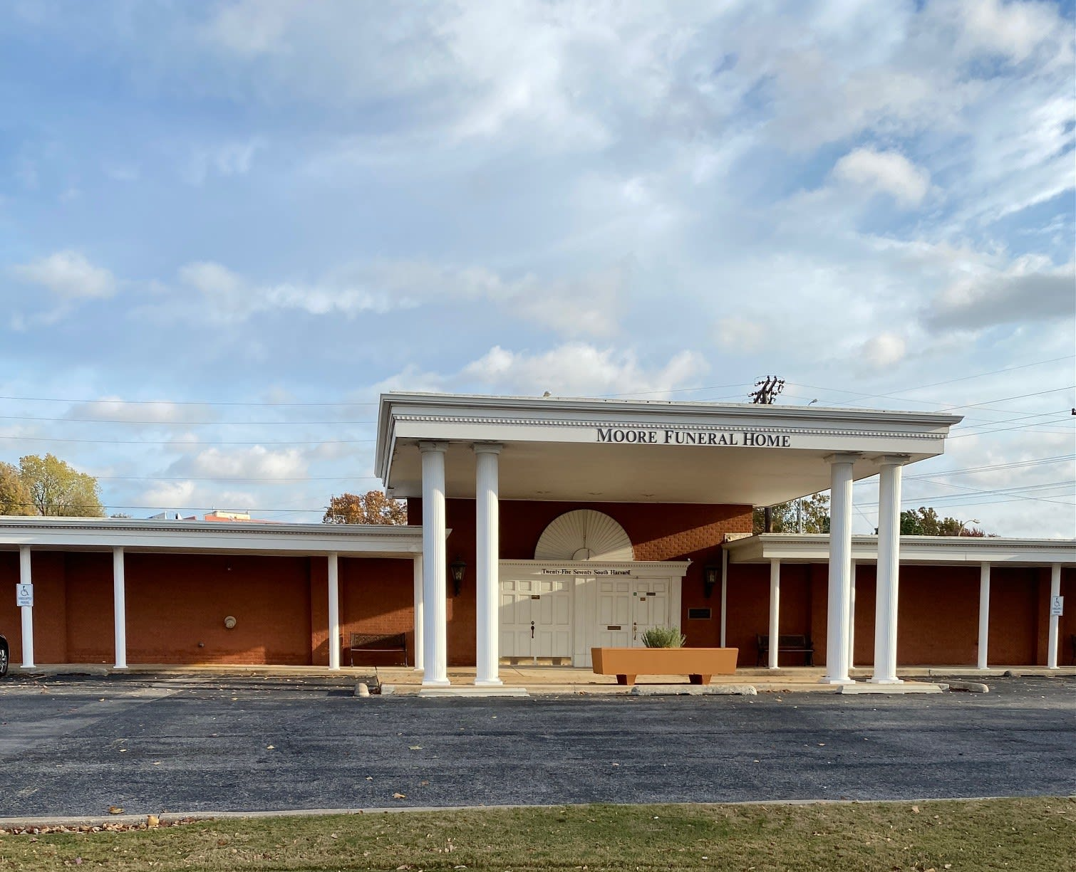 Abandoned brick building with a white covered entrance and cloudy sky overhead