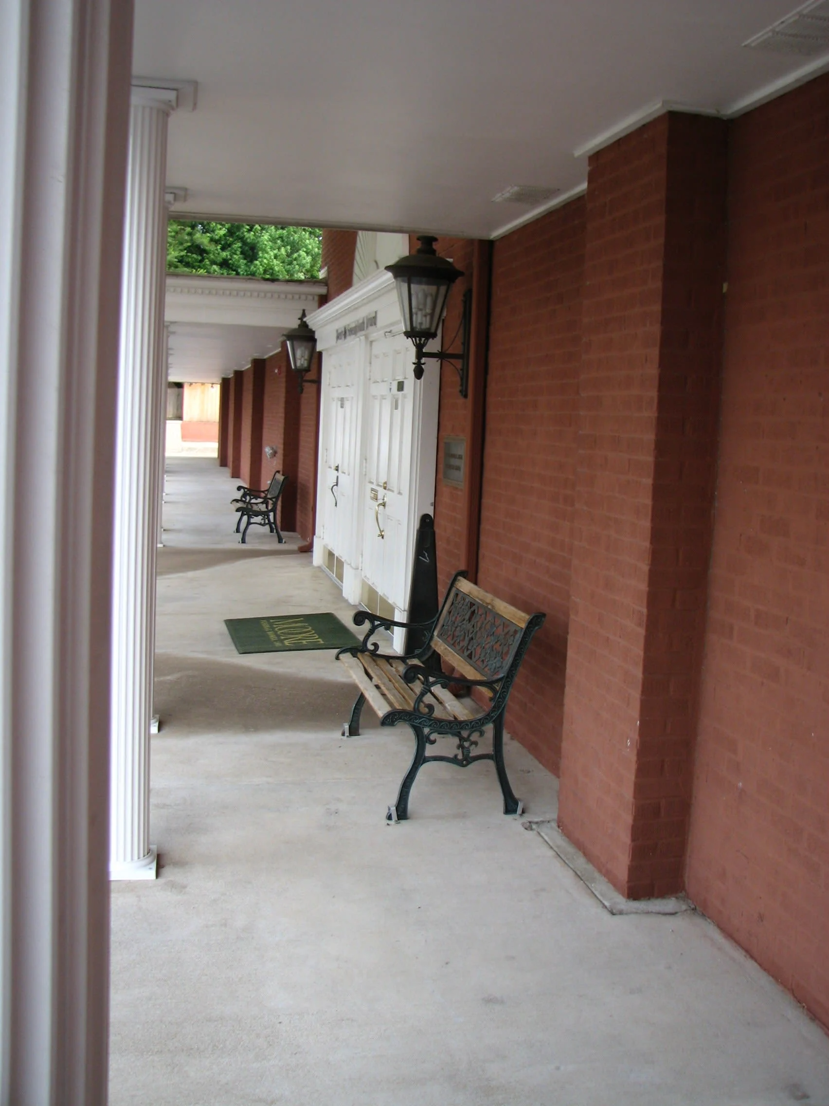 Covered brick walkway with white columns, white door, and a bench along the wall.