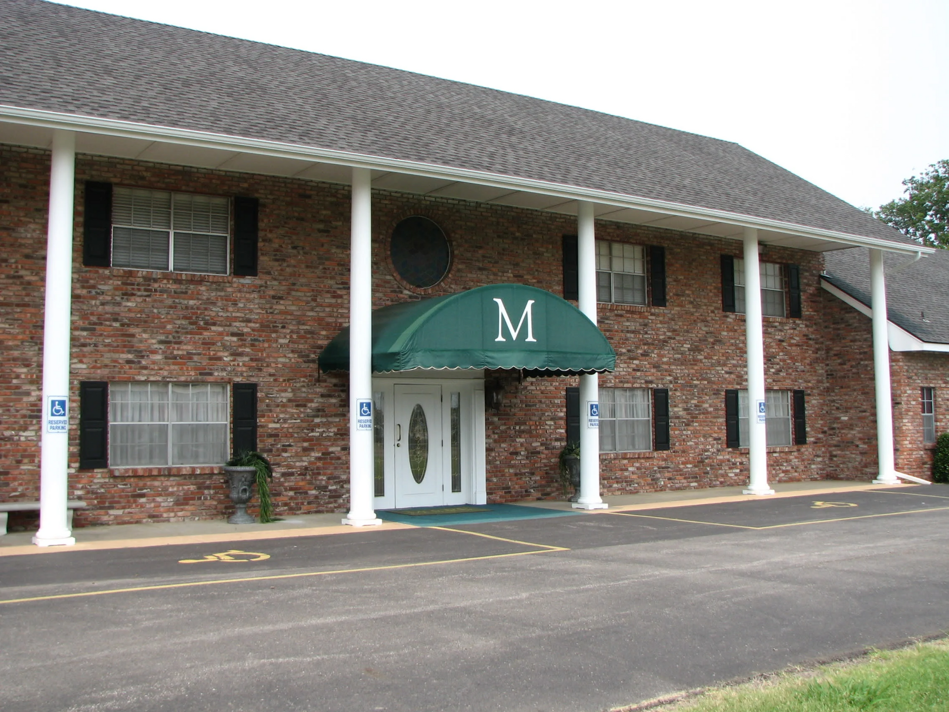 Brick apartment building with green awning and white columns, viewed from the parking lot