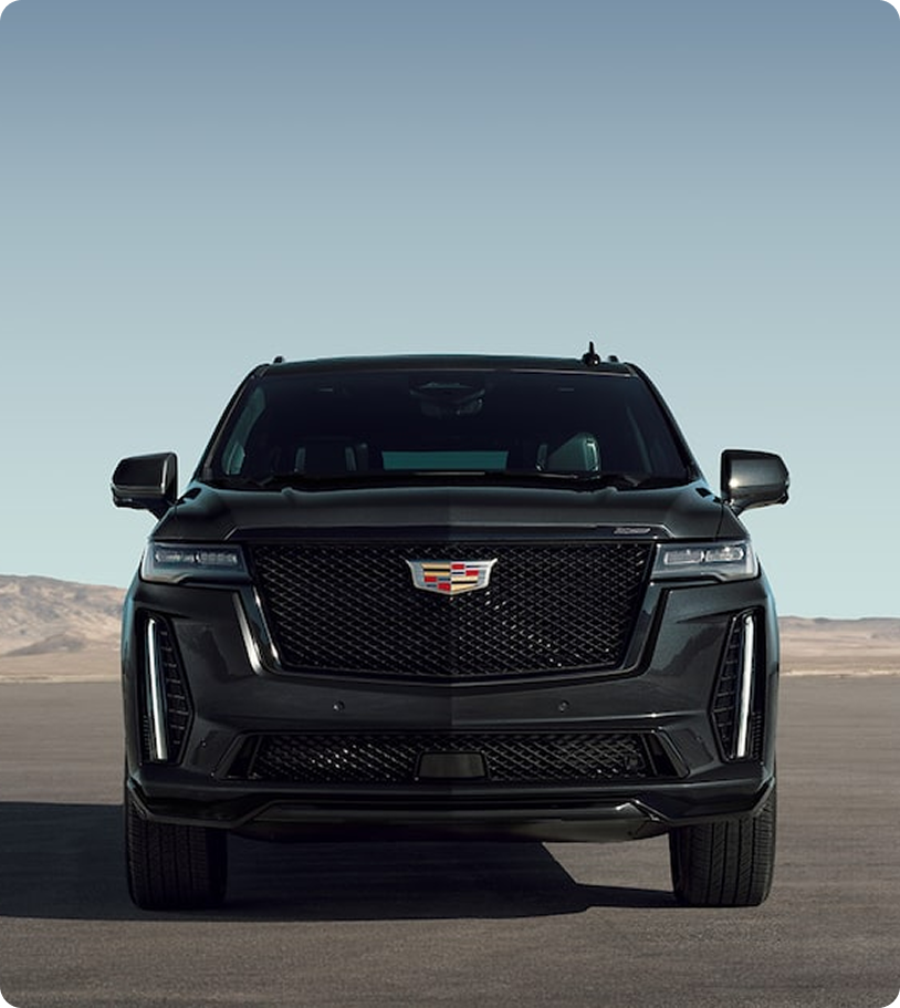 Black Cadillac SUV parked on an open road with desert mountains under a clear sky