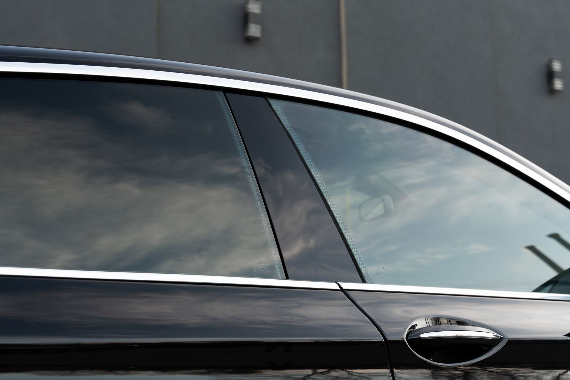 Close-up of a black car door and tinted window against a gray wall.