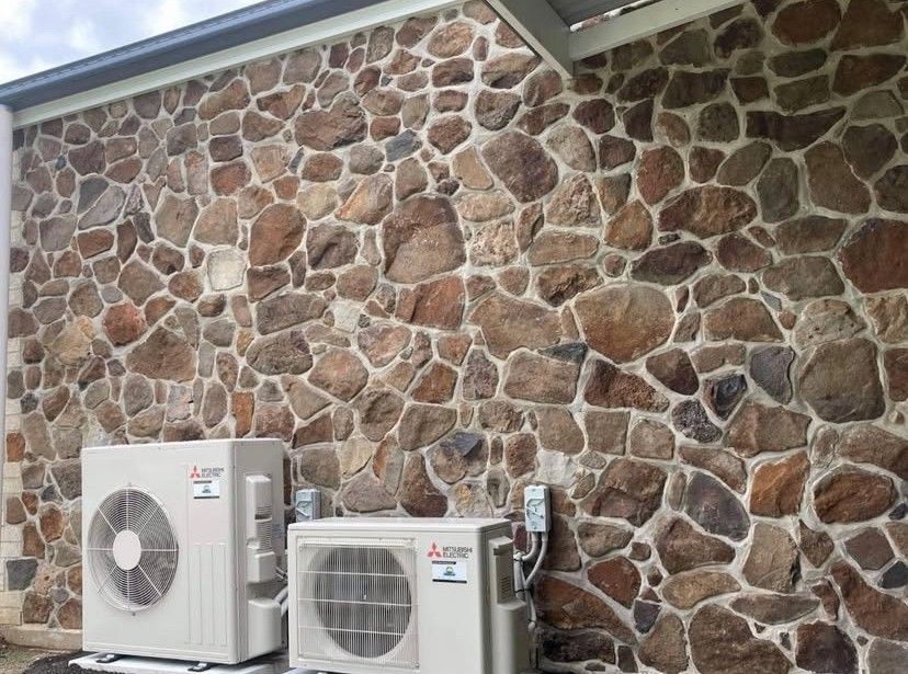 A Air Conditioning Unit Sitting In Front Of A Rock Wall— Frigid-Air PTY Ltd In South Lismore, NSW