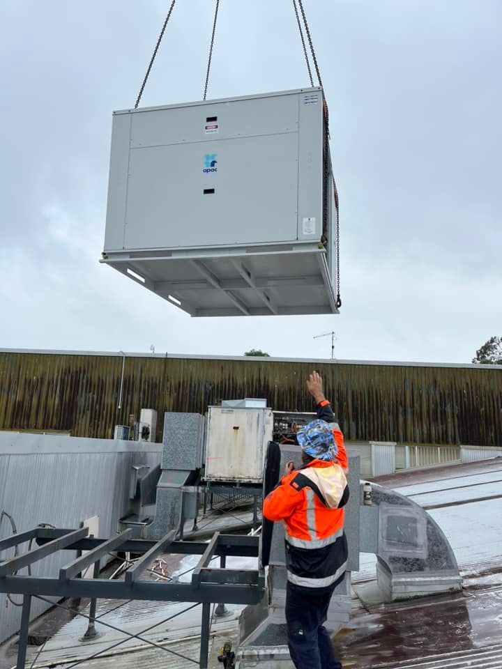 A Man Is Lifting A Large Gray Box From The Roof Of A Building — Frigid-Air PTY Ltd In Lennox Head, NSW