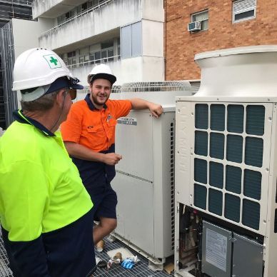 Two Men Wearing Hard Hats Are Standing Next To A Large Air Conditioner — Frigid-Air PTY Ltd In Bangalow, NSW