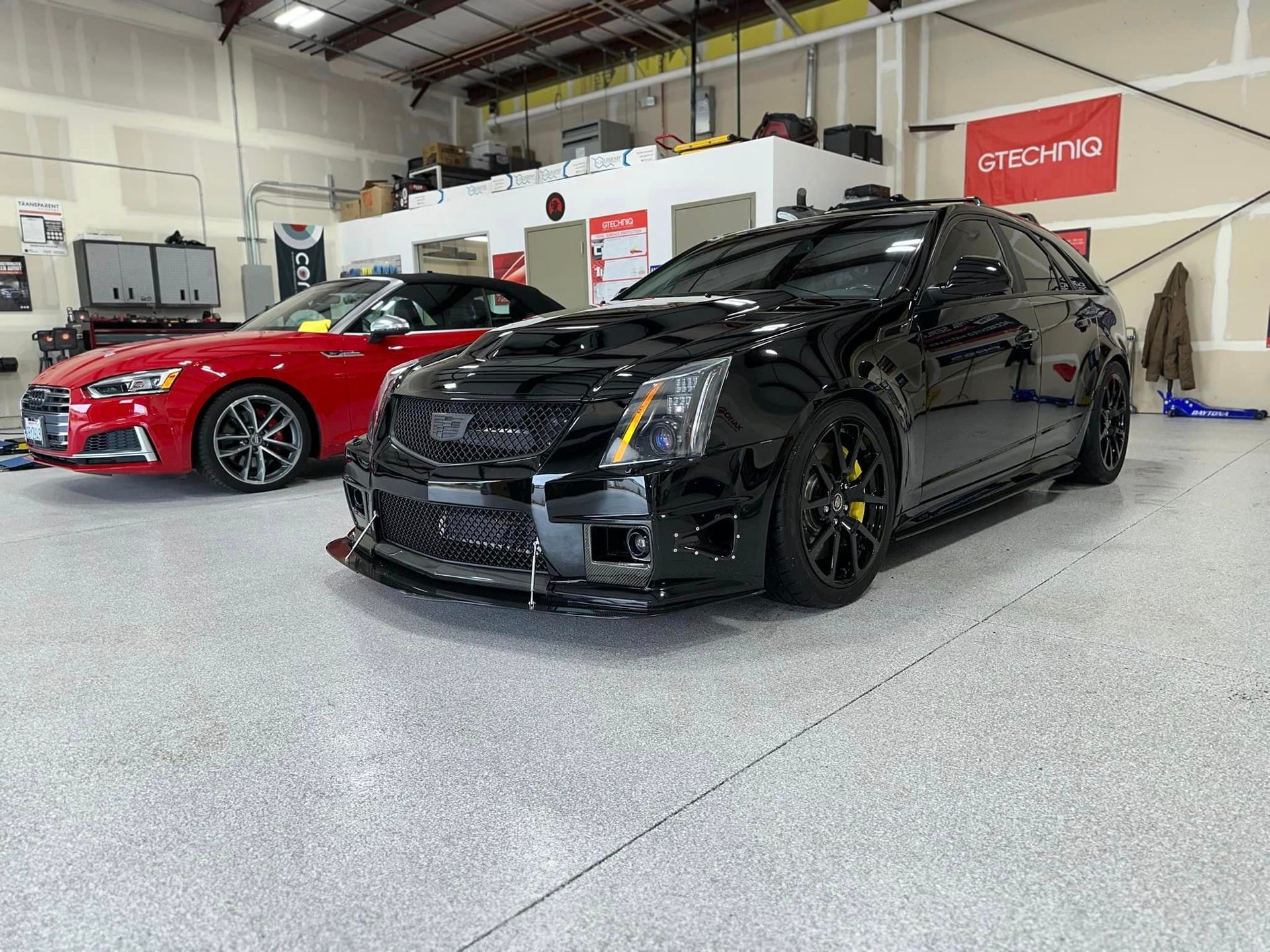 A black car is parked next to a red car in a garage.