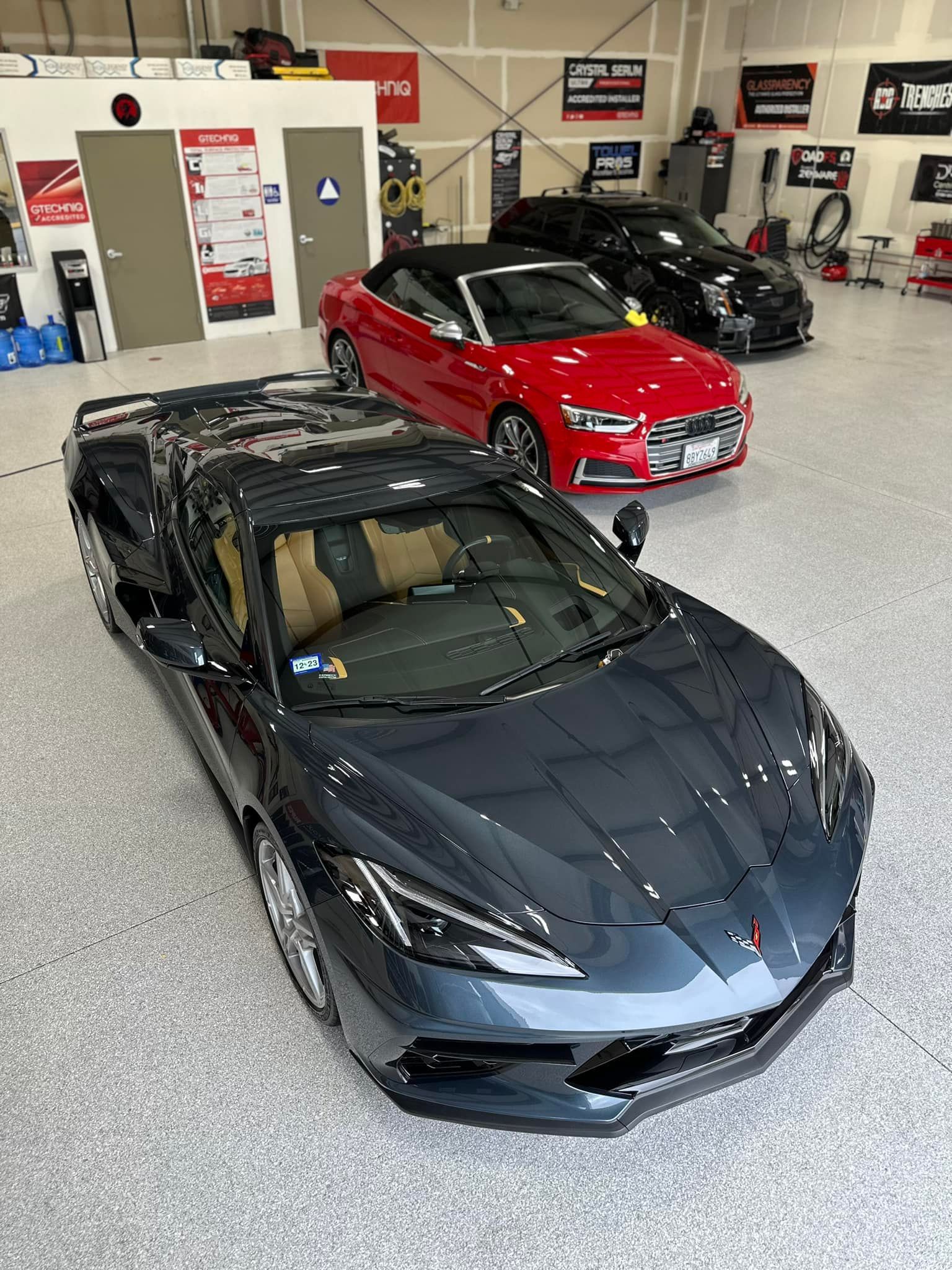 A black corvette convertible is parked in a garage next to a red car.
