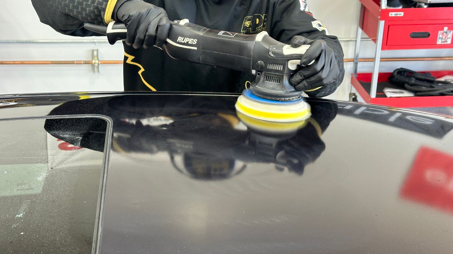 A man is polishing a black car with a machine.