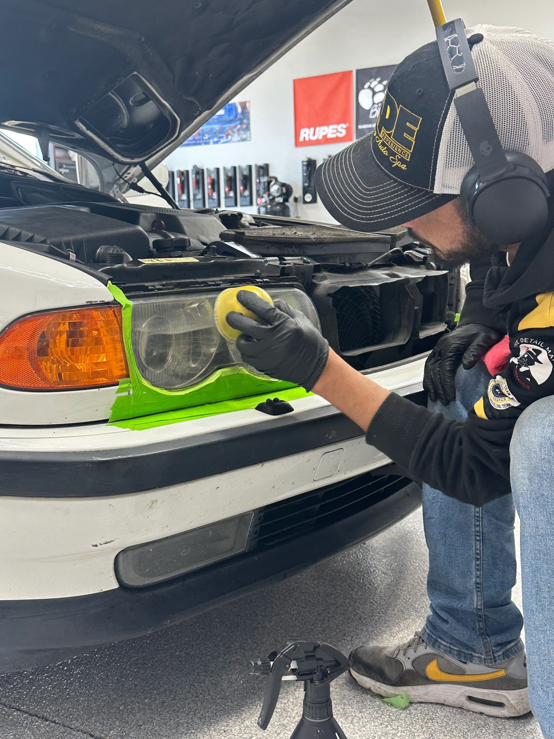 A man is cleaning the headlights of a car in a garage.