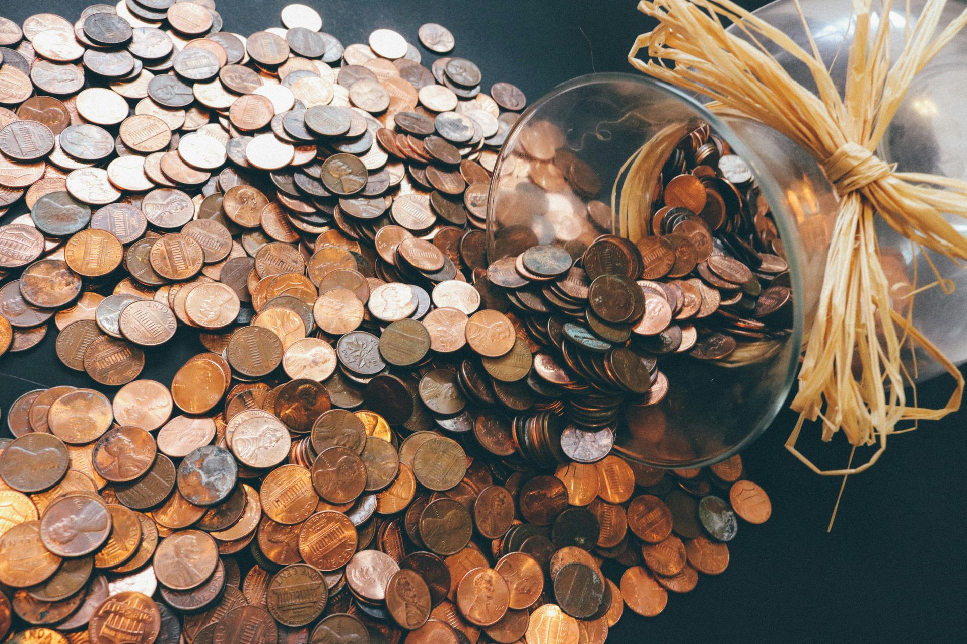 A glass jar filled with coins is sitting on top of a pile of coins.