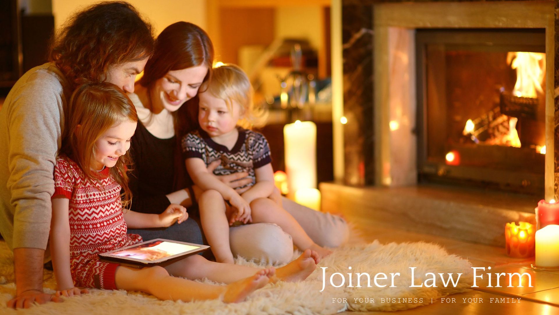 A family is sitting on the floor in front of a fireplace looking at a tablet. A family is sitting on the floor in front of a fireplace looking at a tablet.