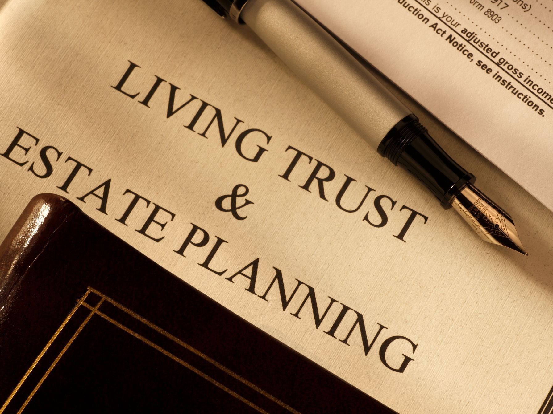A close-up of a "Living Trust & Estate Planning" document with a fountain pen, a leather-bound book, and tax paperwork.