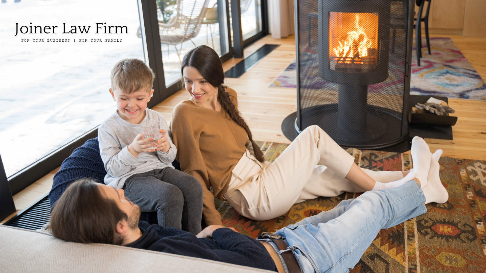 A family is sitting on the floor in front of a fireplace.