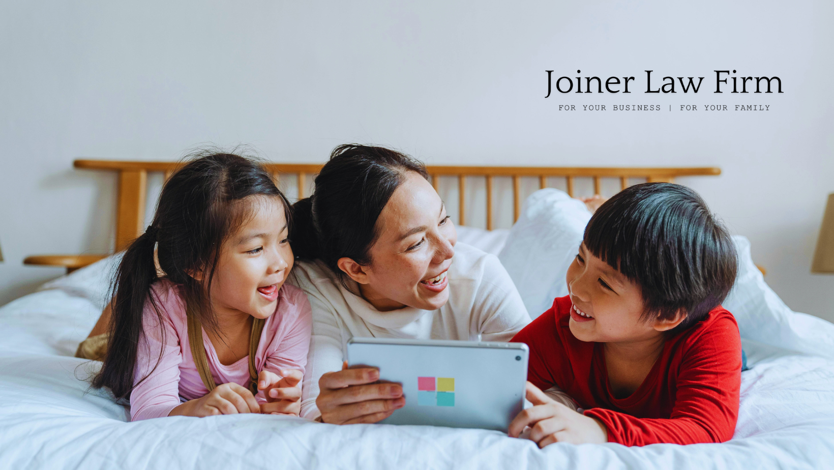 A woman and two children are laying on a bed looking at a tablet. A woman and two children are laying on a bed looking at a tablet.