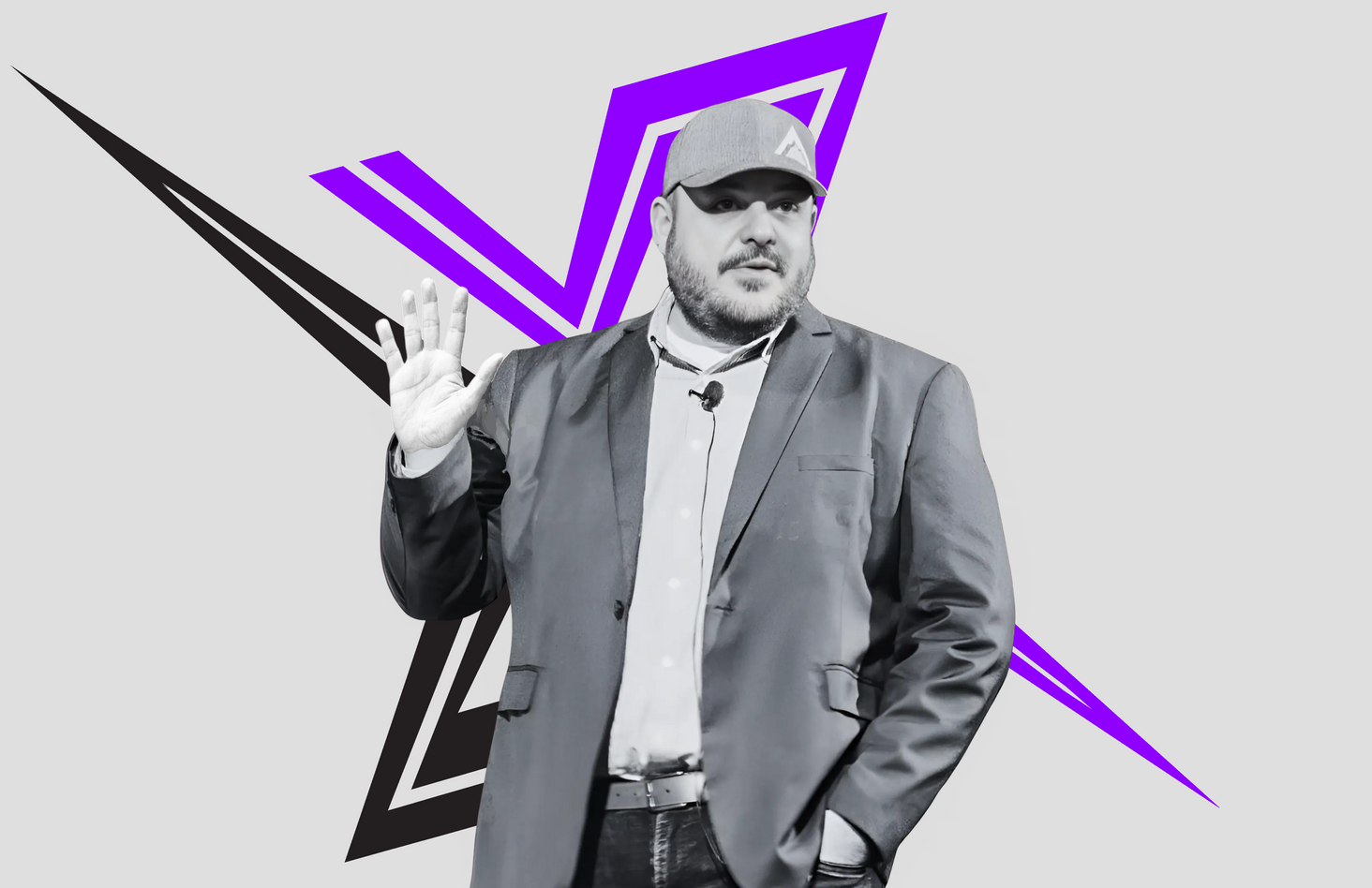 Sean Hamel in gray suit and cap with raised hand, standing before a purple and black geometric backdrop.