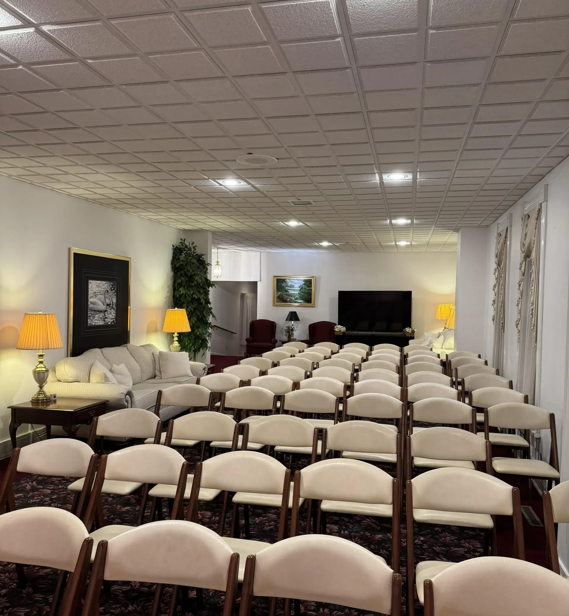 Rows of folding chairs in a room with a couch and lamps