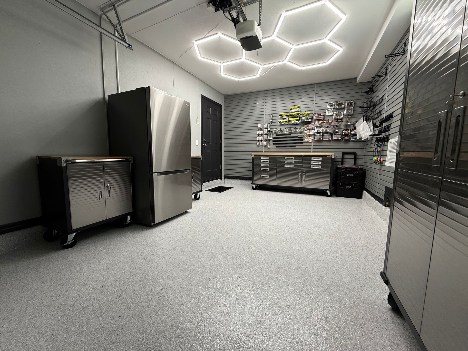 Garage with speckled floor, stainless steel cabinets, appliances, and honeycomb-shaped ceiling lights.