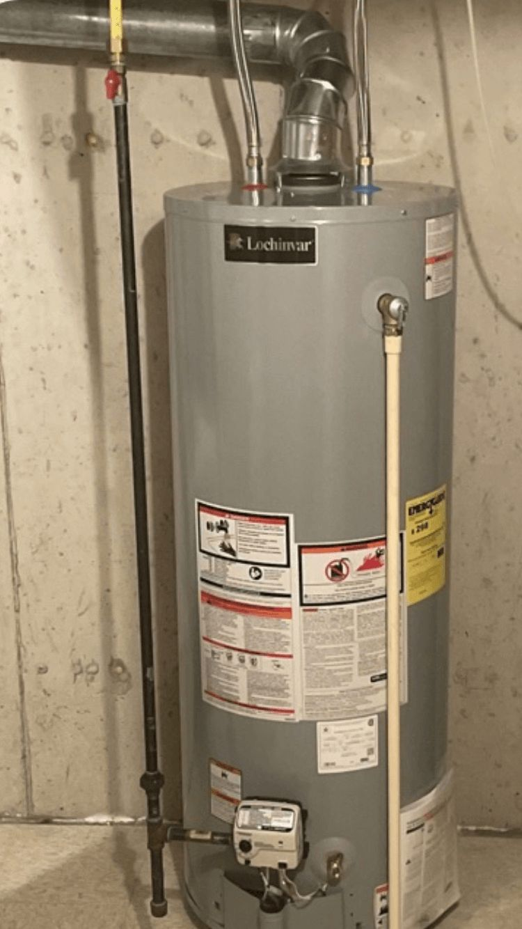 Gray water heater in a utility room with metal vent pipes and warning labels.
