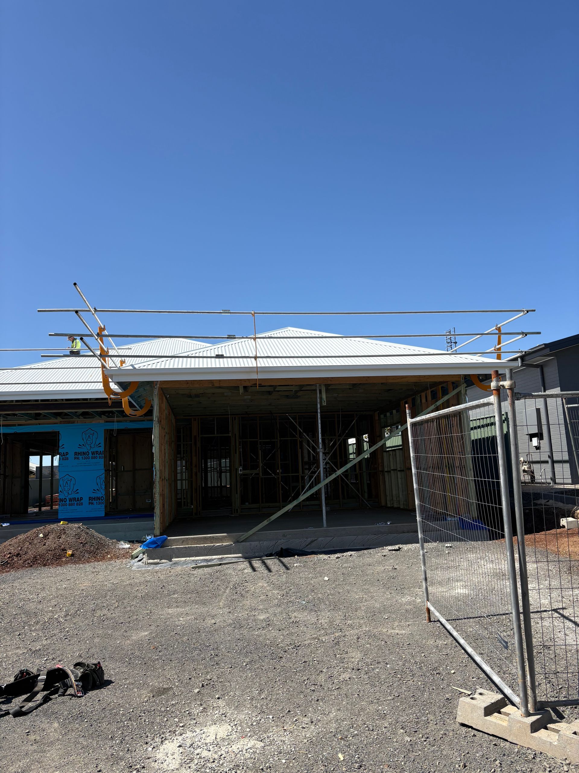 Construction site of a house under a clear, blue sky. Scaffolding supports the roof of a partially built structure.