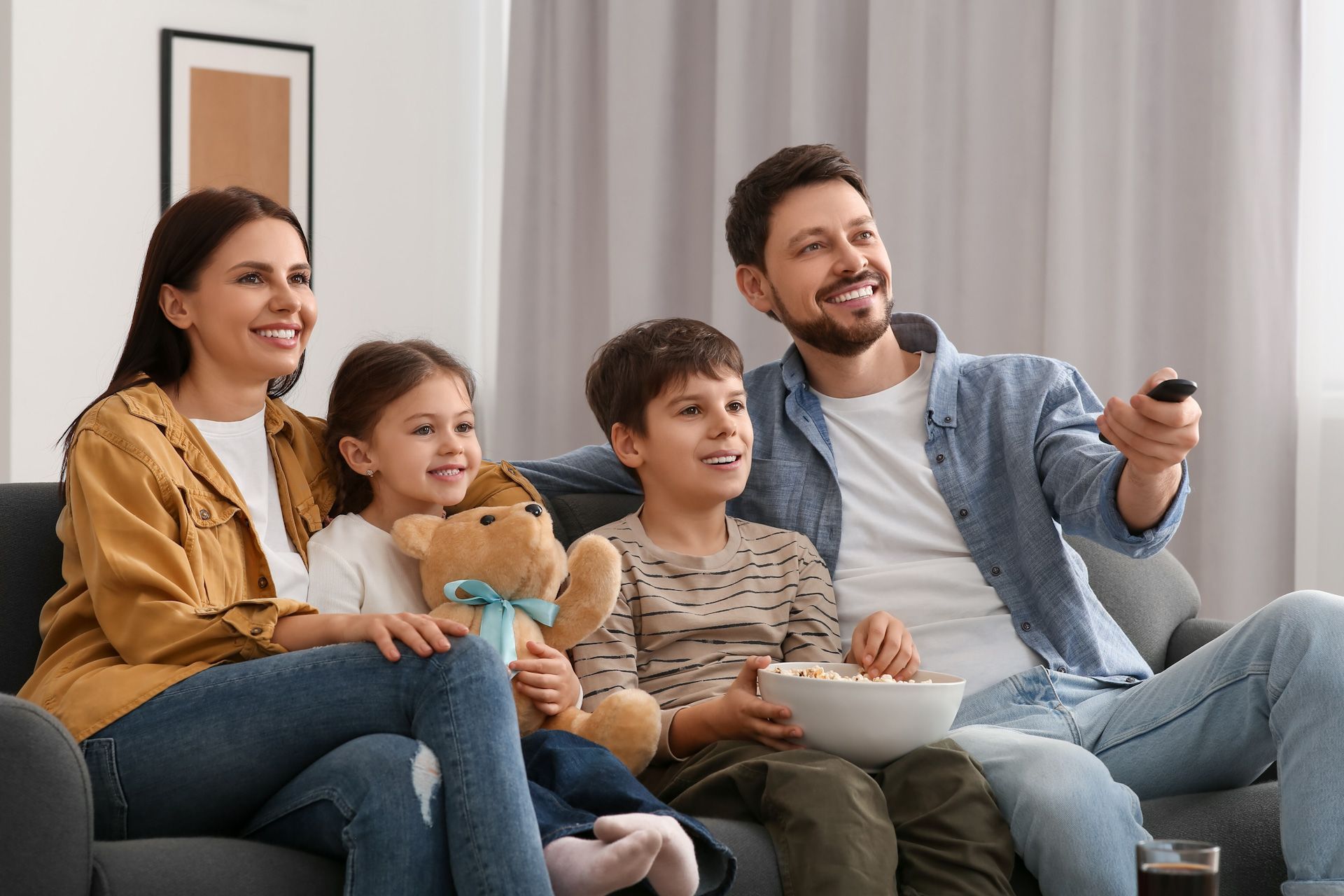 A family sits on a couch eating popcorn and watching tv