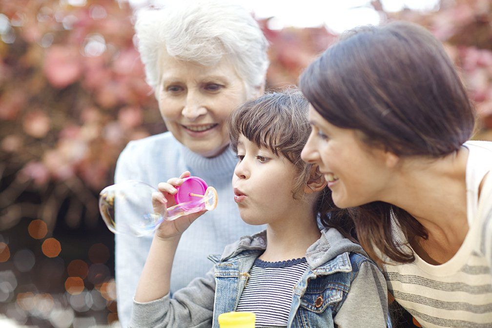 Woman and child blowing bubbles with older woman watching, outdoors.