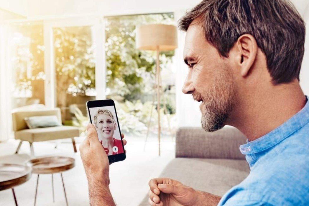 Man on video call with woman on smartphone; indoors, natural light.