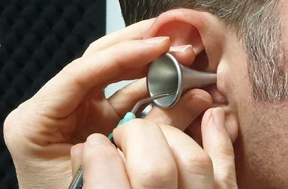 Person's ear being examined with an otoscope, held by two hands in a medical setting.