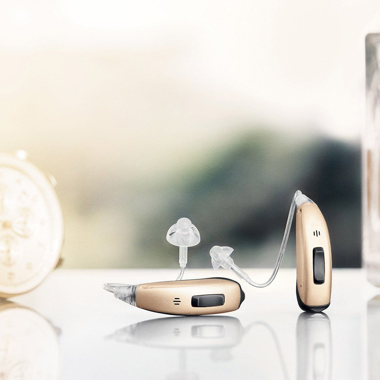 Two beige hearing aids on a reflective surface with a blurred background.