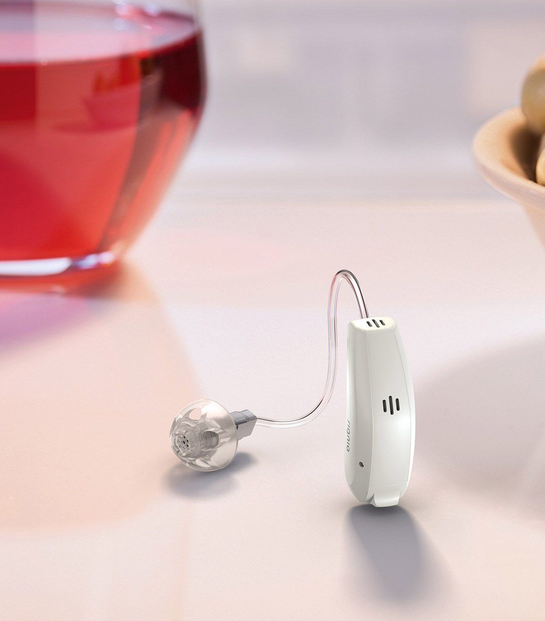 White hearing aid next to a glass of red liquid, presumably wine, on a white surface.