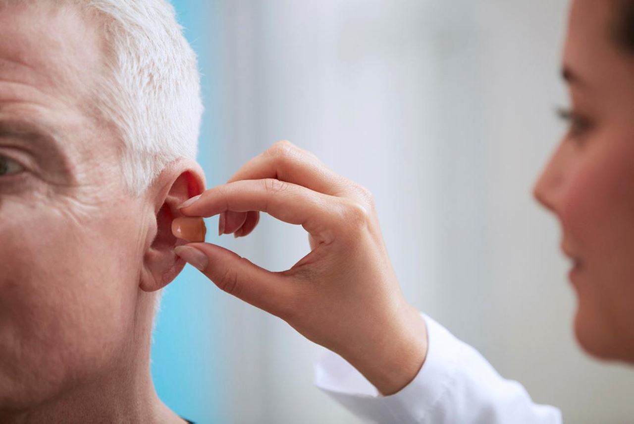 A person having a hearing aid inserted into their ear by a healthcare provider.