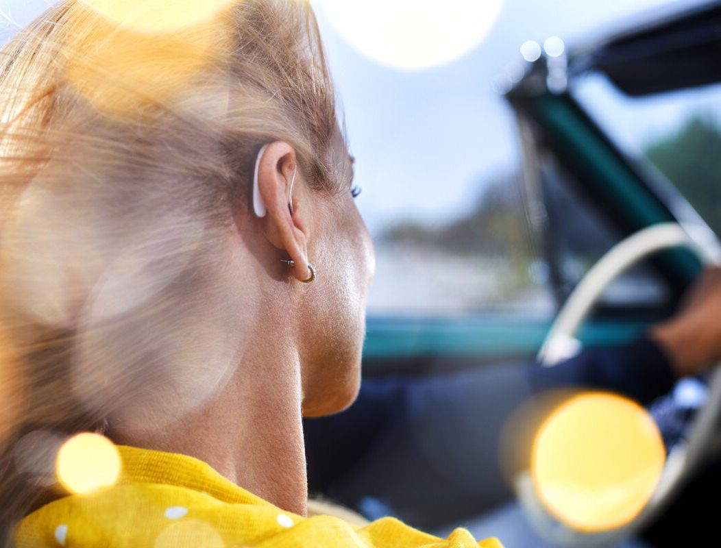 Woman wearing hearing aid in a car with the top down, focus on her ear.