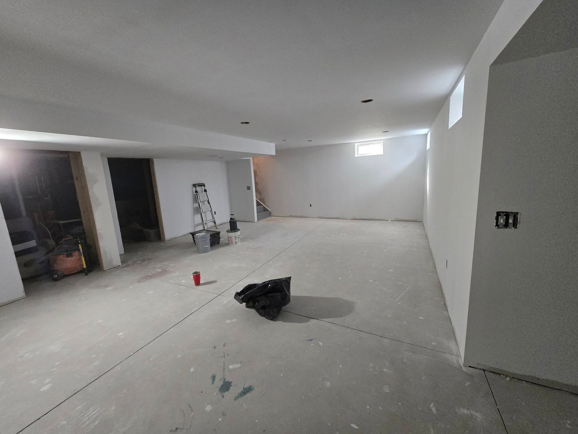 A newly constructed basement with concrete floor and white walls. Construction debris present, including ladder.