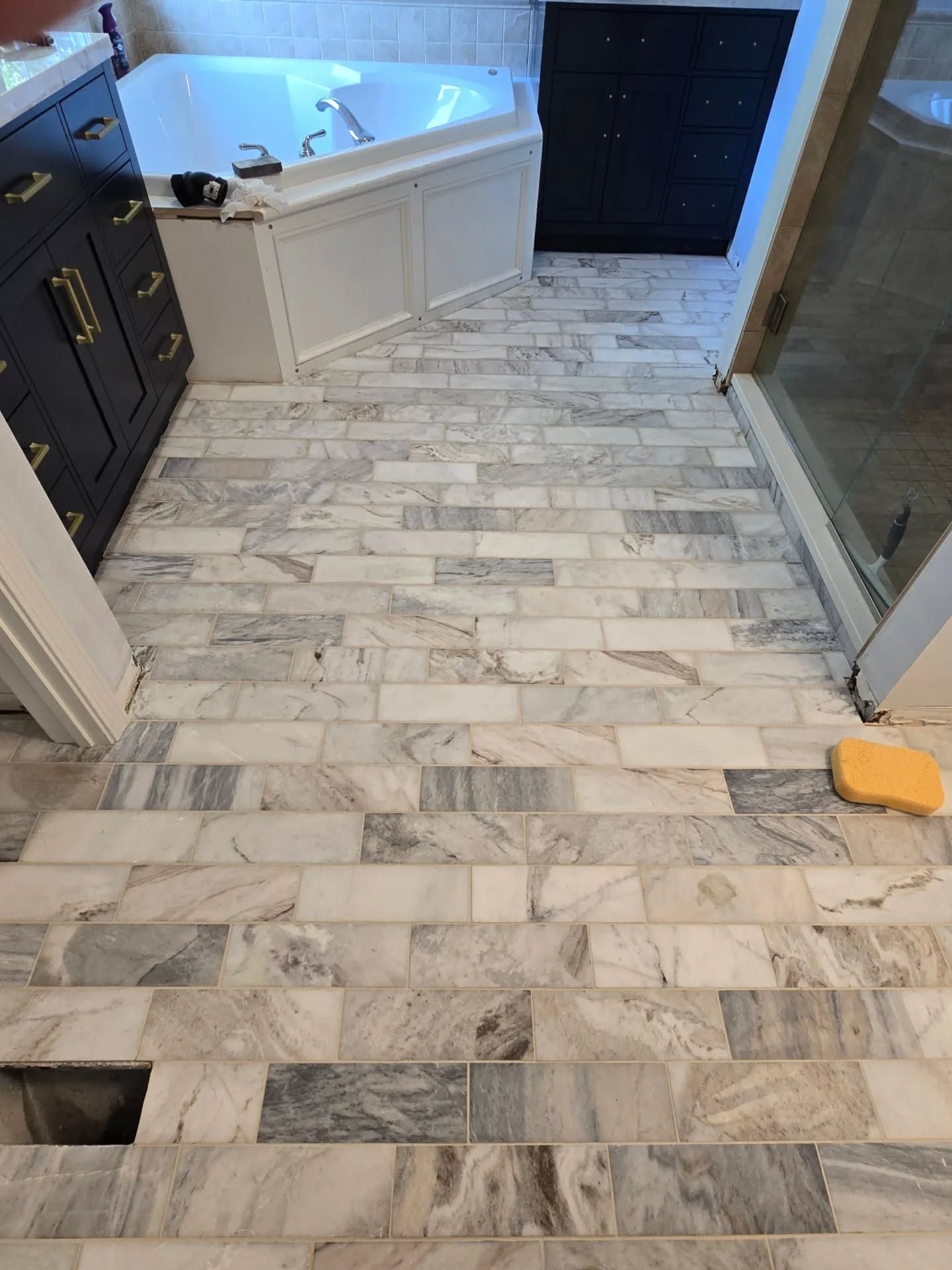 Bathroom floor with marble-like rectangular tiles. White and gray tones, with a bathtub and cabinet visible.