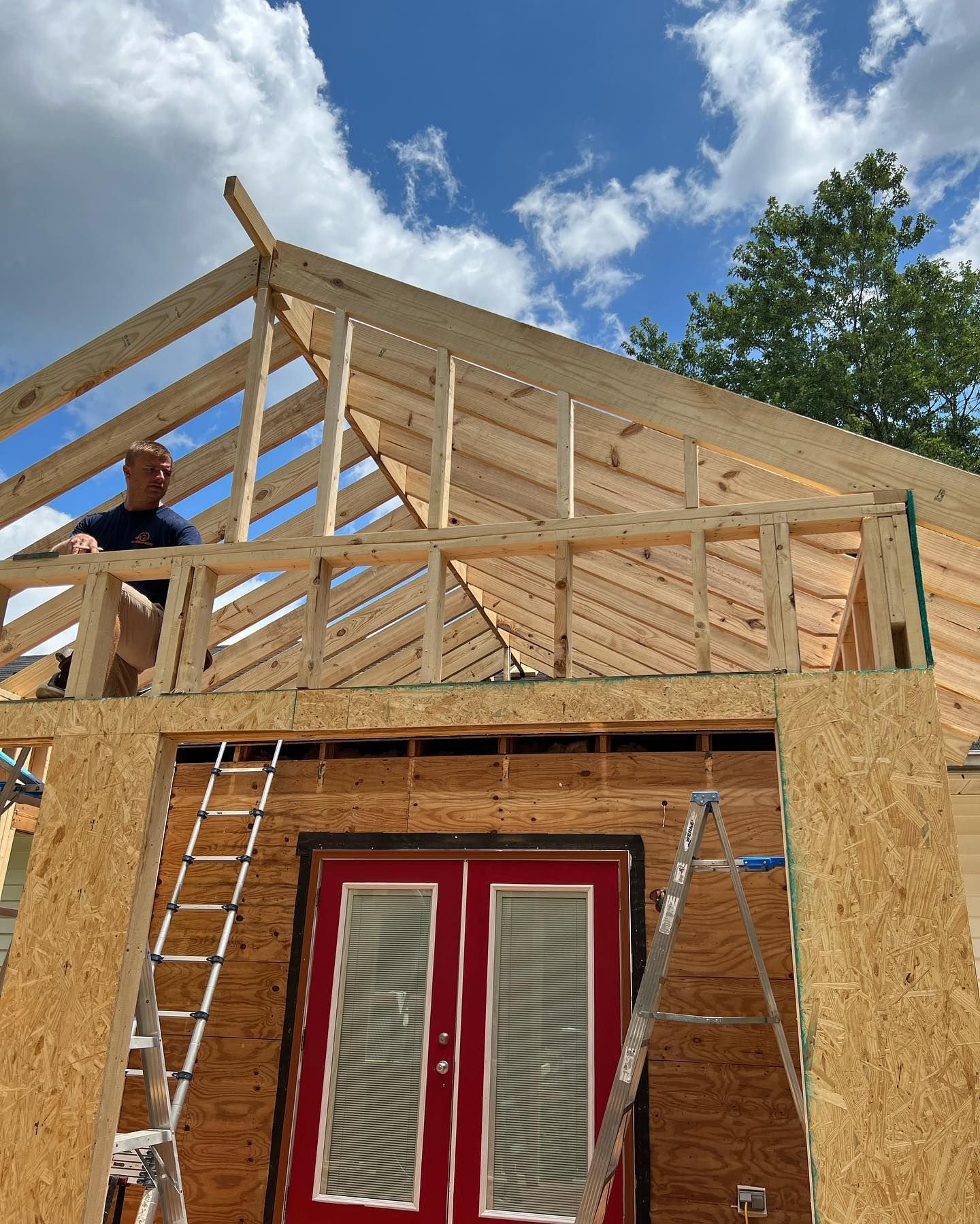 A man is sitting on the roof of a house under construction.